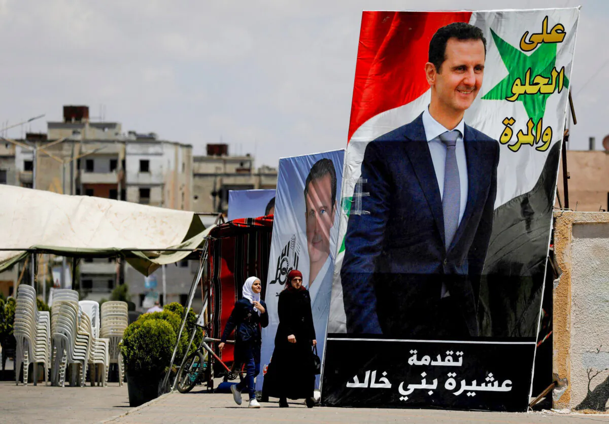 People walk past posters depicting Syria's President Bashar al-Assad, ahead of the May 26 presidential election, in the district of al-Waer in Homs, Syria, on May 23, 2021. (Omar Sanadiki/Reuters)