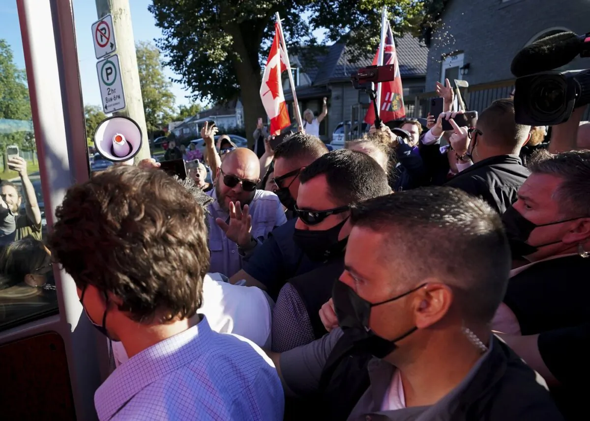 A man (top R) throws gravel at Liberal leader Justin Trudeau (L) as the RCMP security detail provide protection, while protesters shout at a local microbrewery during the Canadian federal election campaign in London Ont., on Sept. 6, 2021. (The Canadian Press/Nathan Denette)