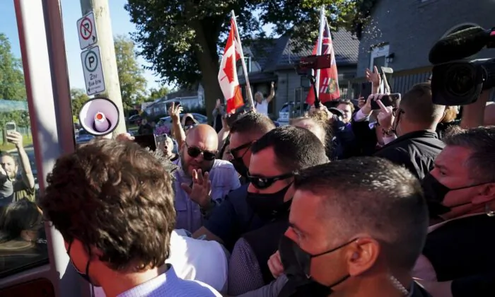 A man (top R) throws gravel at Liberal leader Justin Trudeau (L) as the RCMP security detail provide protection, while protesters shout at a local microbrewery during the Canadian federal election campaign in London Ont., on Sept. 6, 2021. (The Canadian Press/Nathan Denette)