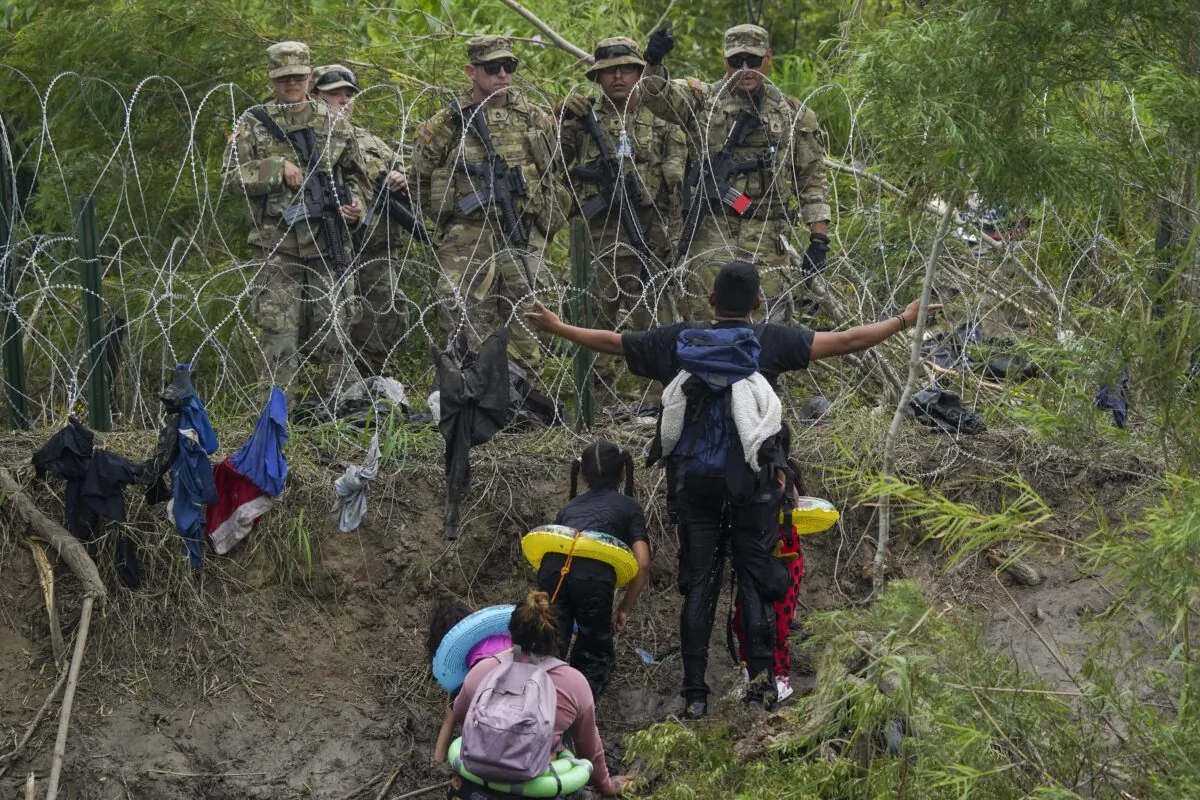 A migrant gestures to Texas National Guards standing behind razor wire on the bank of the Rio Grande river, seen from Matamoros, Mexico, on May 11, 2023. (Fernando Llano/AP Photo)