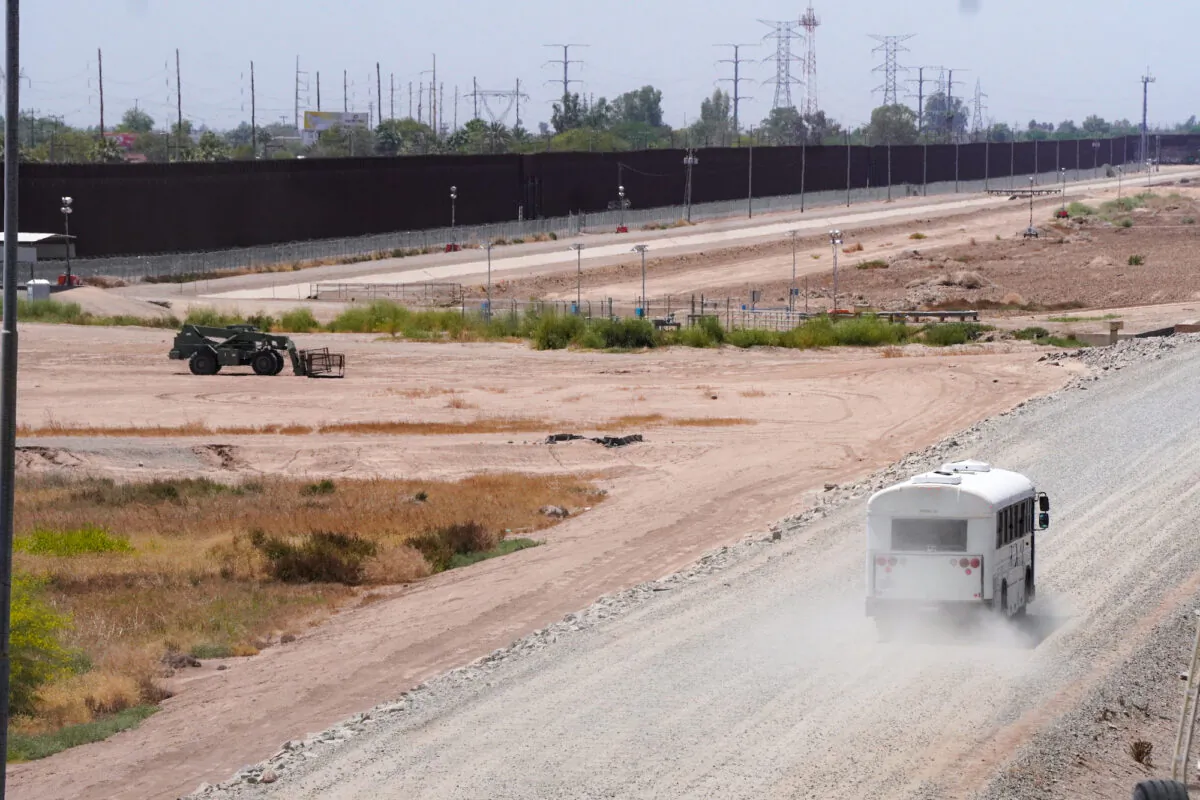 An unmarked bus makes its way along the southern border fence in San Luis, Ariz., ostensibly to retrieved asylum seekers arriving from Mexico. (Allan Stein/The Epoch Times)