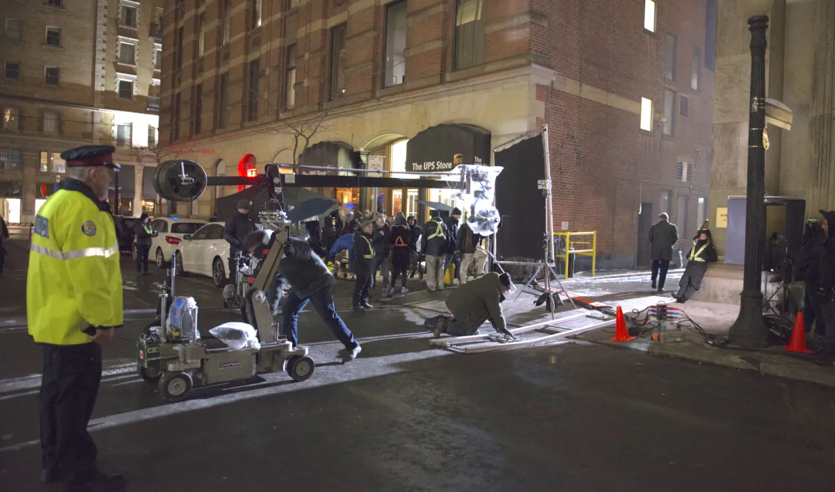 A crew work on a film set on a Toronto street as a police officer looks on, April 17, 2019. (The Canadian Press/Doug Ives)