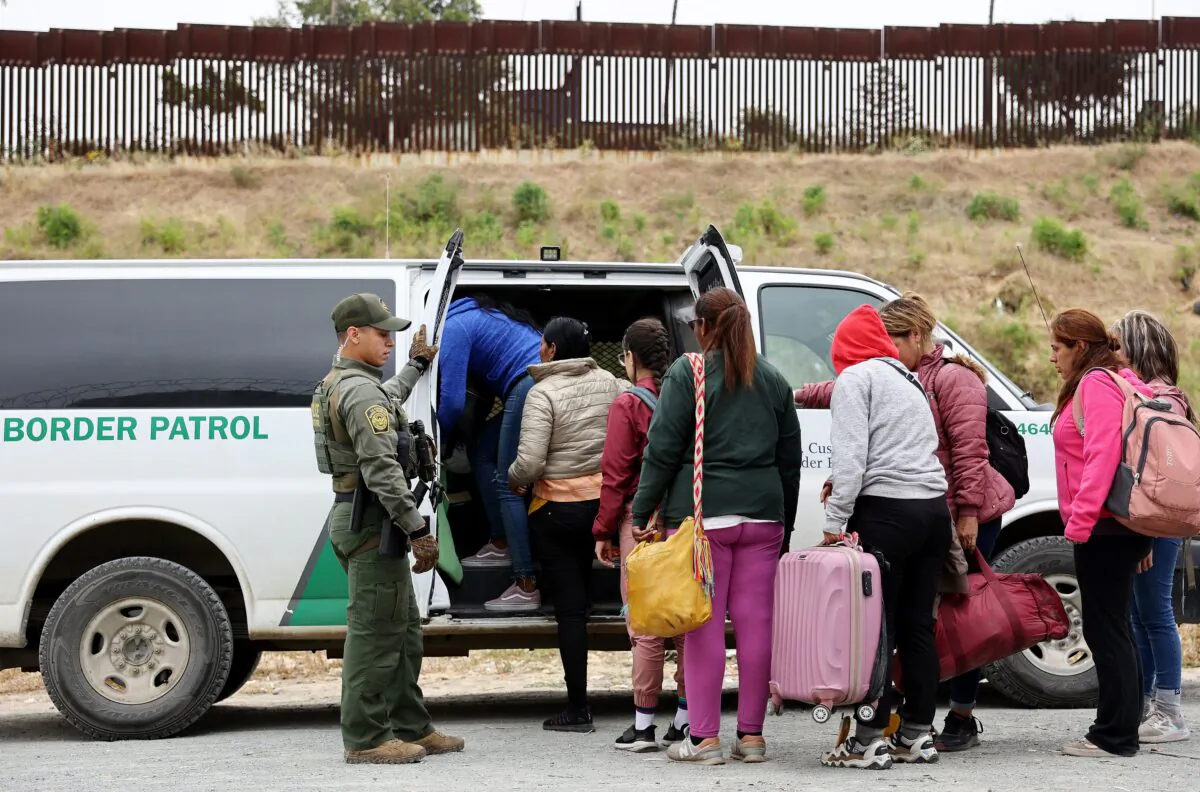 A U.S. Border Patrol agent keeps watch as migrants enter a vehicle to be transported from a makeshift camp between border walls between the U.S. and Mexico in San Diego on May 13, 2023. (Mario Tama/Getty Images)