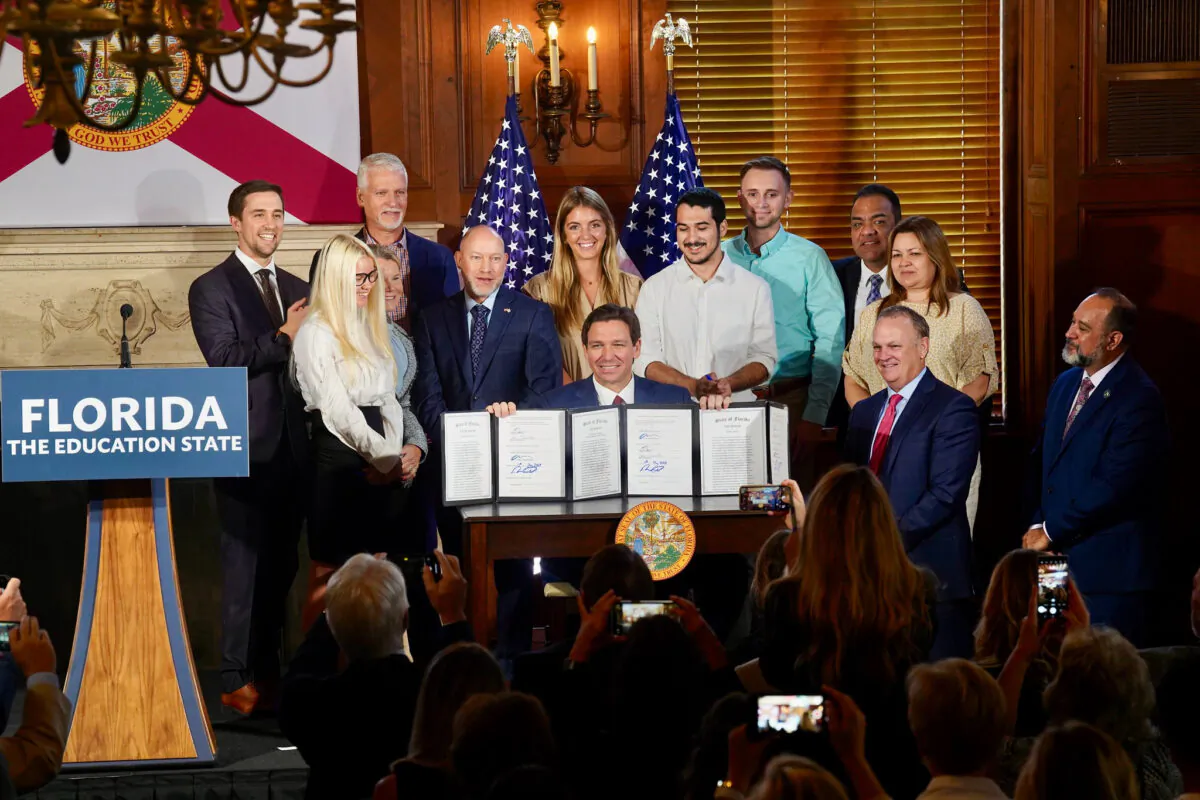 Florida Gov. Ron DeSantis holds up three just-signed bills related to higher education in the state—including one that bans diversity, equity, and inclusion (DEI) practices—at New College in Sarasota on May 15, 2023. (Courtesy of the Florida Governor's Office)