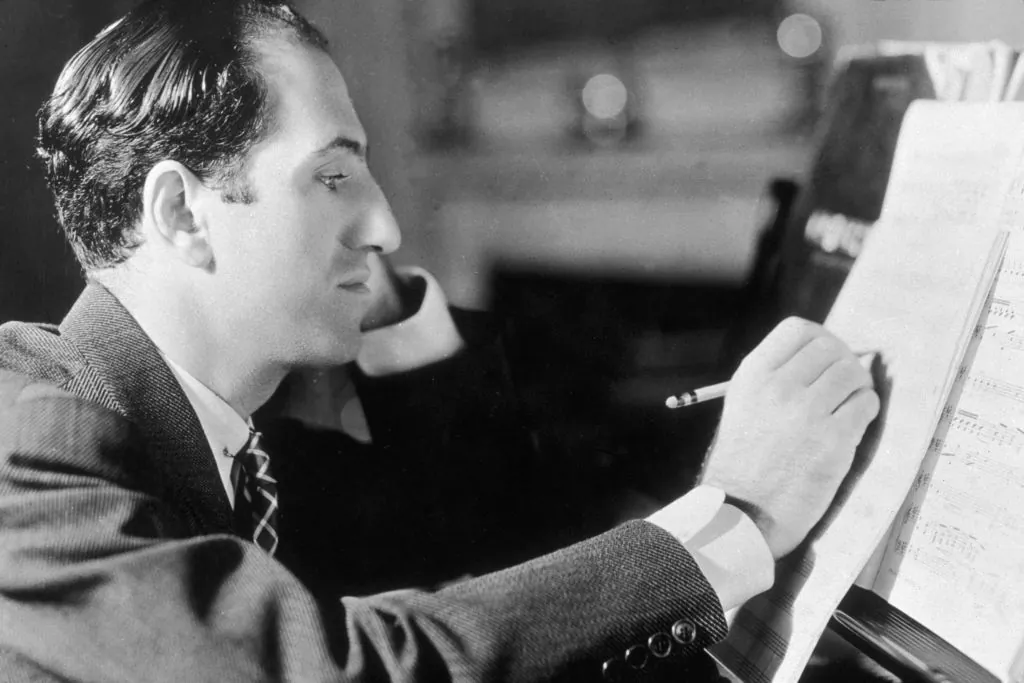 Profile headshot of American composer George Gershwin (1898–1937) writing notes on a musical score while sitting at his piano, New York City. (Hulton Archive/Getty Images)