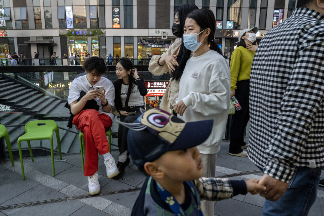 A couple look at a mobile phone as they wait outside a restaurant for a table in a retail shopping area in Beijing, China, on April 18, 2023. (Kevin Frayer/Getty Images)
