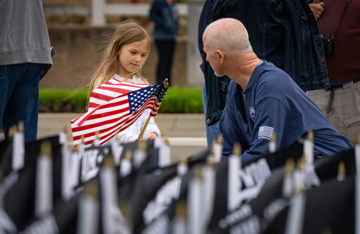 Ellie Paxton, 5, stands with her grandfather Jim Linehan amongst dozens of POW flags in Yorba Linda, Calif., on May 23, 2023. (John Fredricks/The Epoch Times)