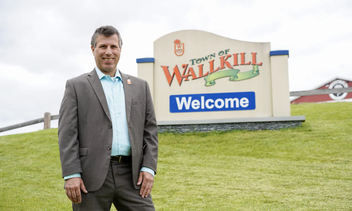 Neil Meyer in front of a welcome sign along Route 211 in the Town of Wallkill, N.Y., on May 19, 2023. (Cara Ding/The Epoch Times)