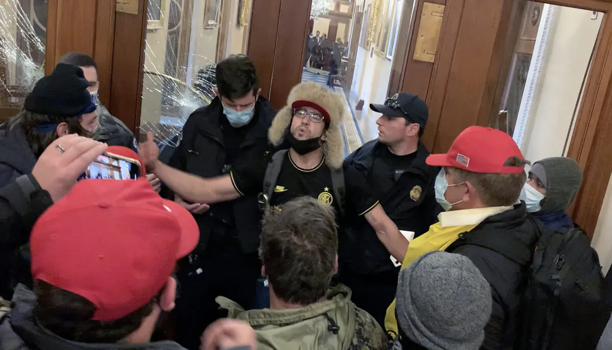 Christopher Grider (at right with yellow flag draped in front) just before he hands a riot helmet to Zachary Alam outside the Speaker's Lobby at the U.S. Capitol on Jan. 6, 2021. (Sam Montoya/For The Epoch Times)