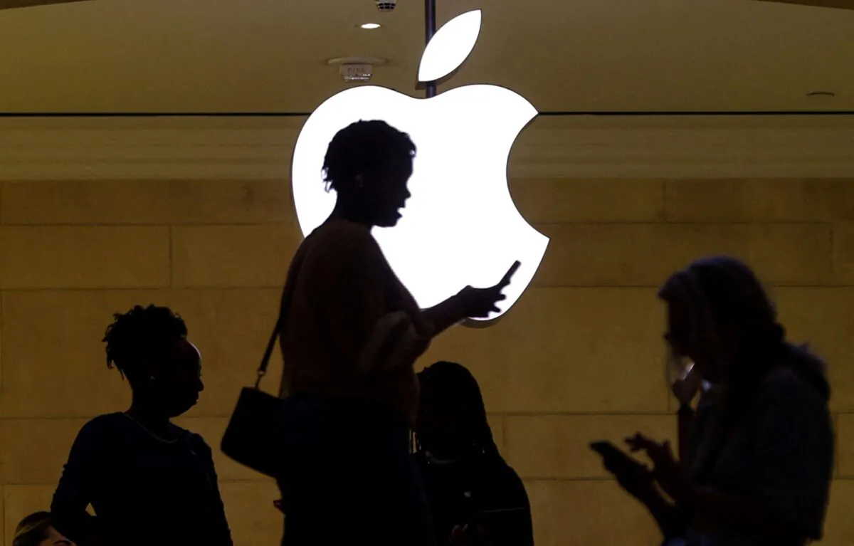 A women uses an iPhone mobile device as she passes a lighted Apple logo at the Apple store at Grand Central Terminal in New York on April 14, 2023. (Mike Segar/Reuters)