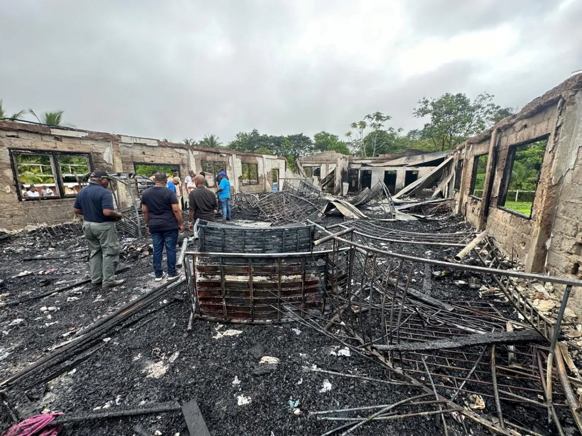People stand inside the remains of a burnt secondary school dormitory after several children died after a fire gutted the building overnight, in Mahdia, Guyana, on 22 May, 2023. (Guyana Presidency/Handout via Reuters)