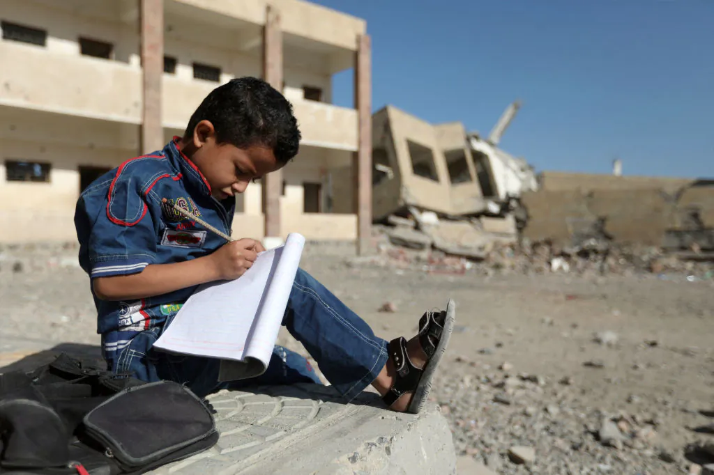 A Yemeni boy school writes as he sits outside a school that was damaged in an air strike in the southern Yemeni city of Taez, on March 16, 2017. (Ahmad Al-Basha/AFP via Getty Images)