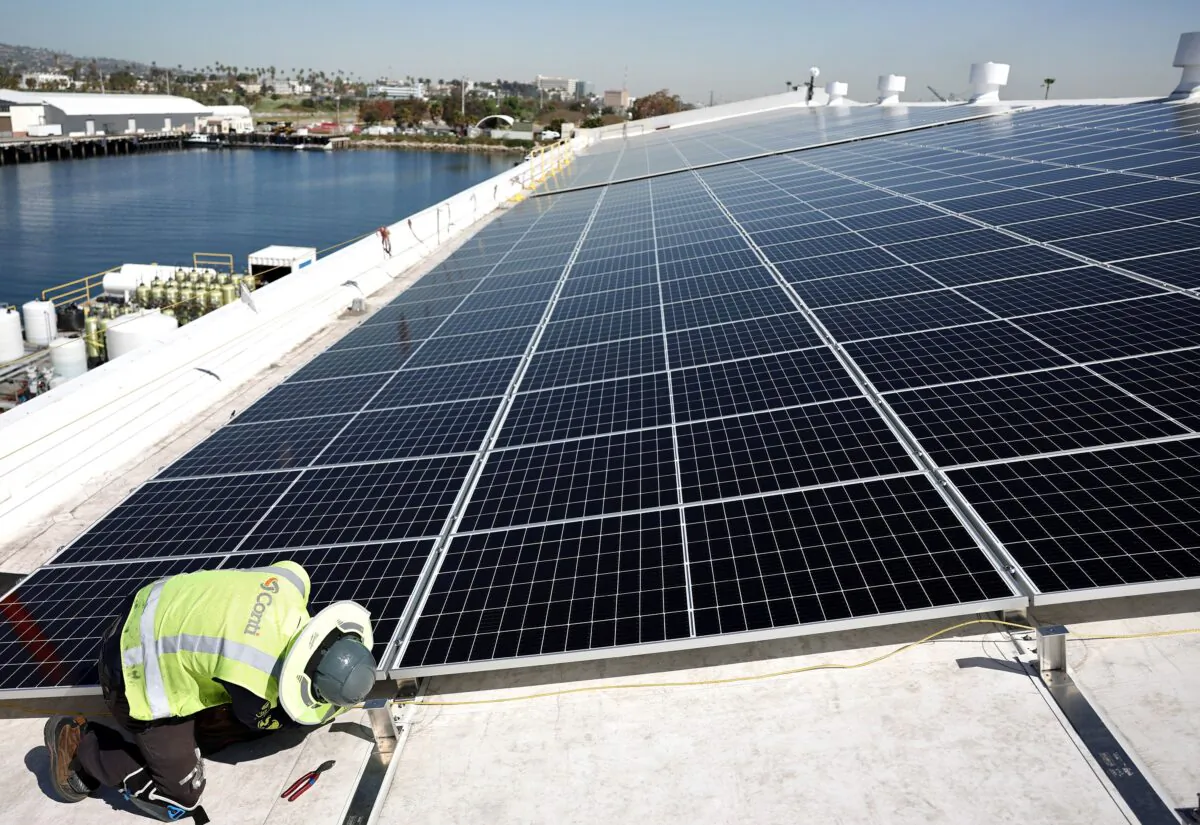 A worker installs solar panels during the completion phase of a 4-acre solar rooftop atop AltaSea's research and development facility at the Port of Los Angeles, in the San Pedro neighborhood, in Los Angeles, Calif., on April 21, 2023. (Mario Tama/Getty Images)