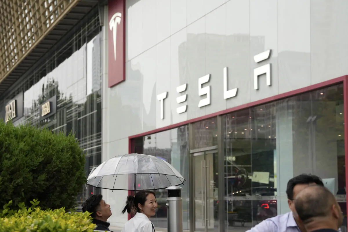 Workers chat under an umbrella outside the Tesla showroom in Beijing, China, on May 30, 2023. (AP Photo/Ng Han Guan)