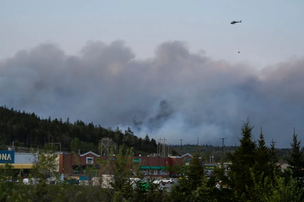 A helicopter carrying water flies over heavy smoke from an out-of-control fire in a suburban community outside of Halifax that spread quickly, engulfing multiple homes and forcing the evacuation of local residents on May 28, 2023. (Darren Calabrese/The Canadian Press)