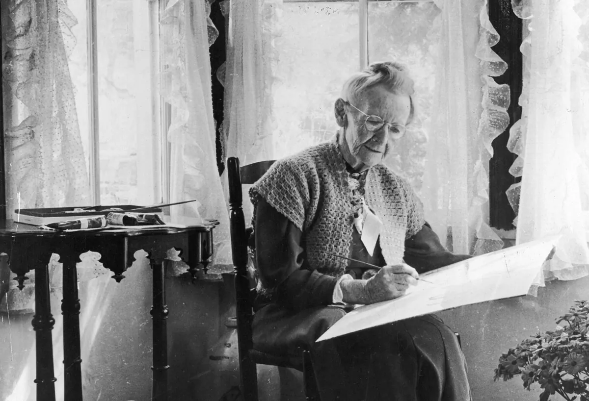 Grandma Moses paints while seated in a rocking chair in front of a window, 1950s. (Archive Photos/Getty Images)