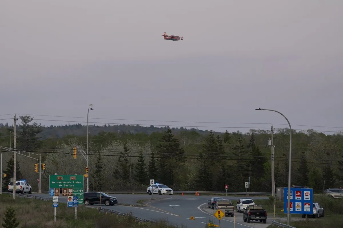 A water bomber plane flies over a RCMP roadblock as smoke fills the sky from an out-of-control fire in a suburban community outside of Halifax that quickly spread, engulfing multiple homes and forcing the evacuation of local residents on May 28, 2023. (The Canadian Press/Darren Calabrese)