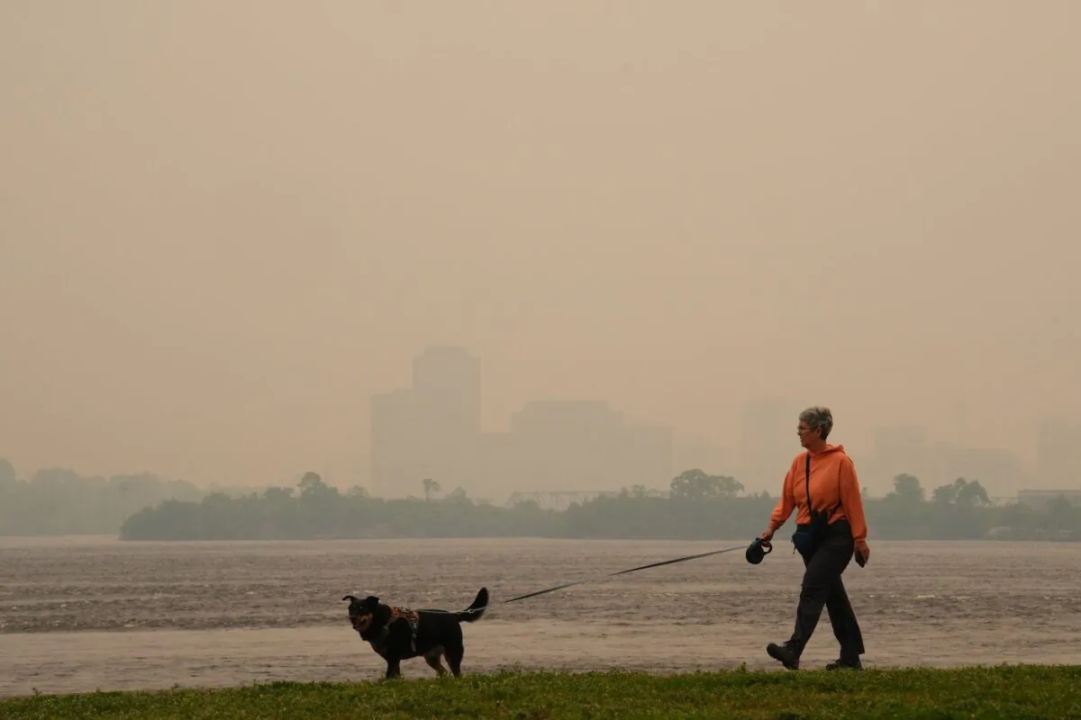 A woman walks her dog along the Ottawa River in Ottawa as smoke from wildfires obscures Gatineau, Que., in the distance on June 6, 2023. (The Canadian Press/Sean Kilpatrick)
