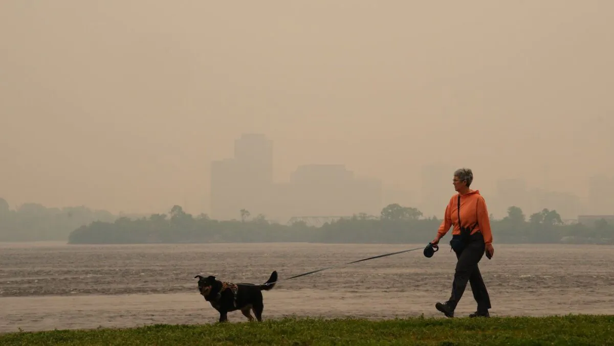 A woman walks her dog along the Ottawa River in Ottawa as smoke from wildfires obscures Gatineau, Que., in the distance on June 6, 2023. (The Canadian Press/Sean Kilpatrick)