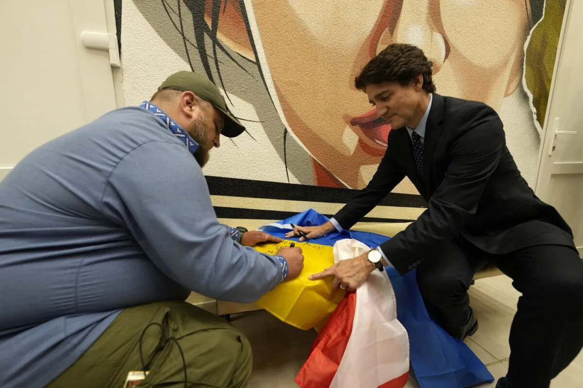 Canadian Prime Minister Justin Trudeau, right, holds a Ukrainian flag as a veteran writes a note during a tour of a military hospital in Kyiv, Ukraine on June 10, 2023. (The Canadian Press/Frank Gunn)
