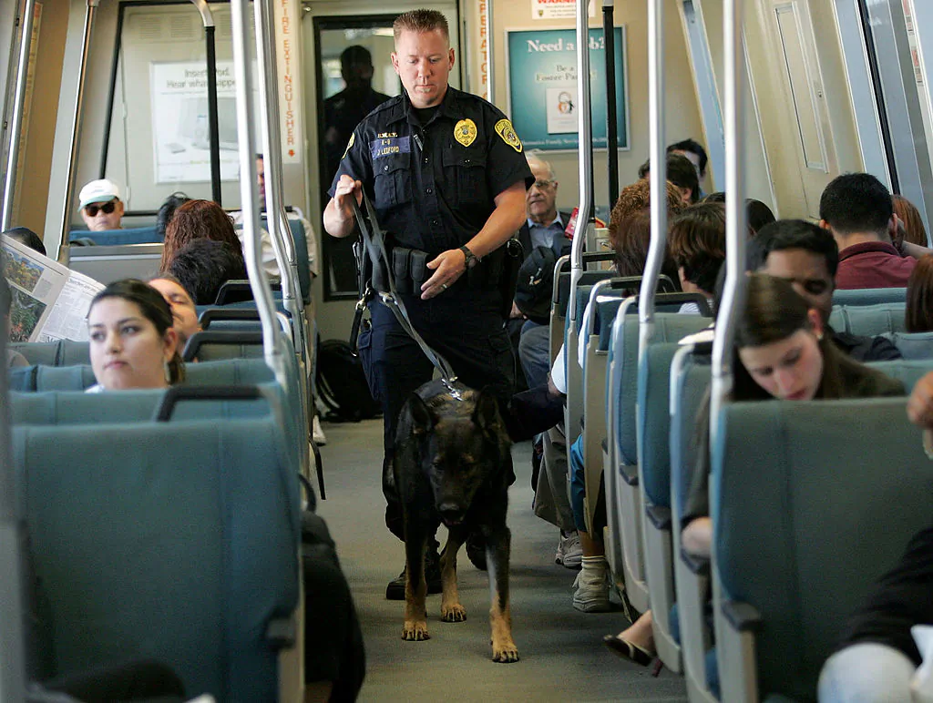 Bay Area Rapid Transit police officer Jason Ledford patrols with his bomb-sniffing dog Andy while on aboard a BART train August 11, 2005 in Oakland, Calif. BART remains at a heightened state of alert following the recent London Underground bombings and is preparing to launch a poster campaign in its stations that encourage riders to report suspicious packages and activity. (Photo by Justin Sullivan/Getty Images)