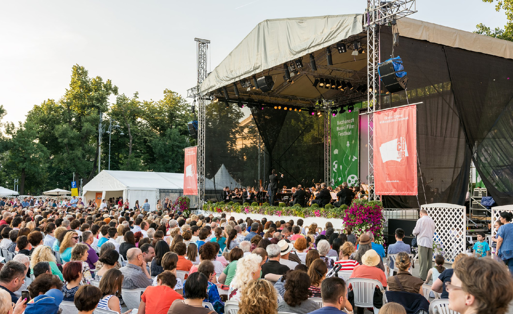 A large outdoor seated crowd listening to an orchestra