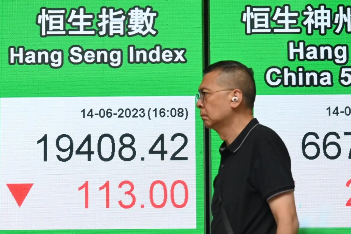A Hong Kong resident walks past an electronic display board showing the Hang Seng Index, on June 14, 2023. (Bill Cox/The Epoch Times)