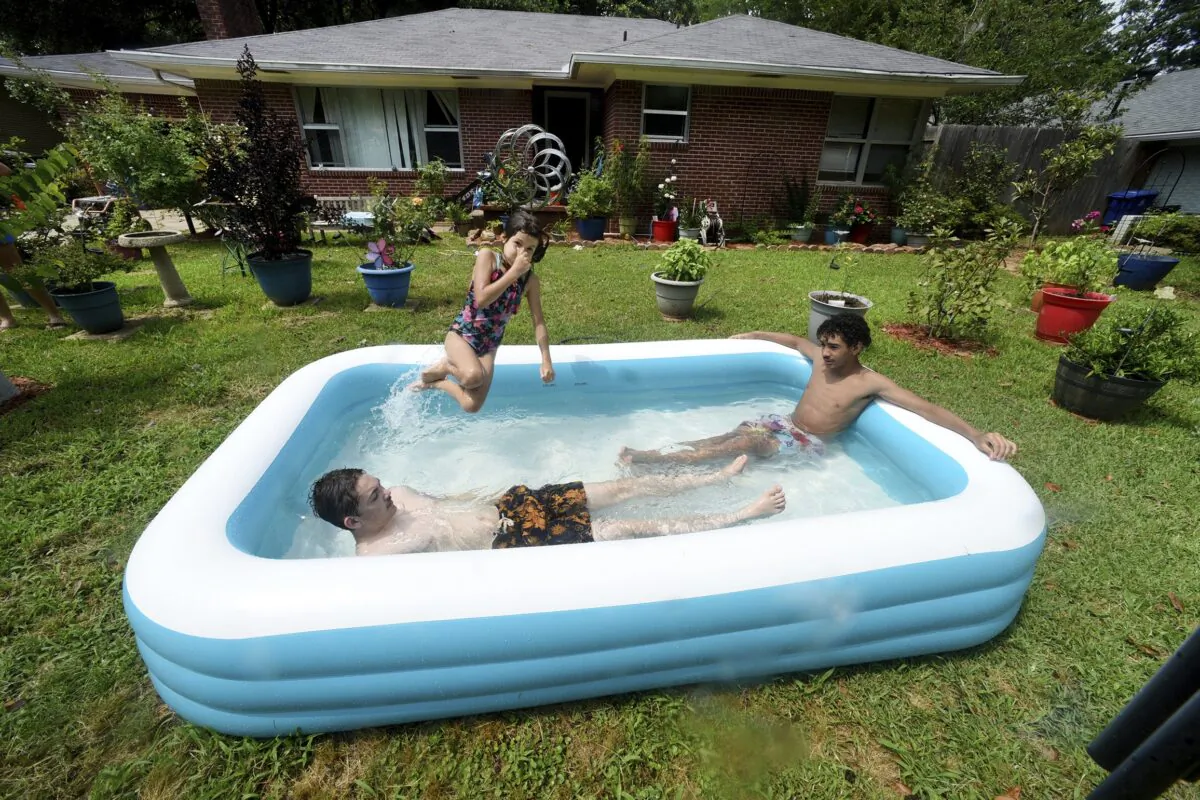 (L–R) Cason Bullis, Mya Kampfer, and Caleb Dessos find a way to cool off with their inflatable pool in the front yard of their house in Shreveport, La., on June 17, 2023. (Henrietta Wildsmith/The Shreveport Times via AP)