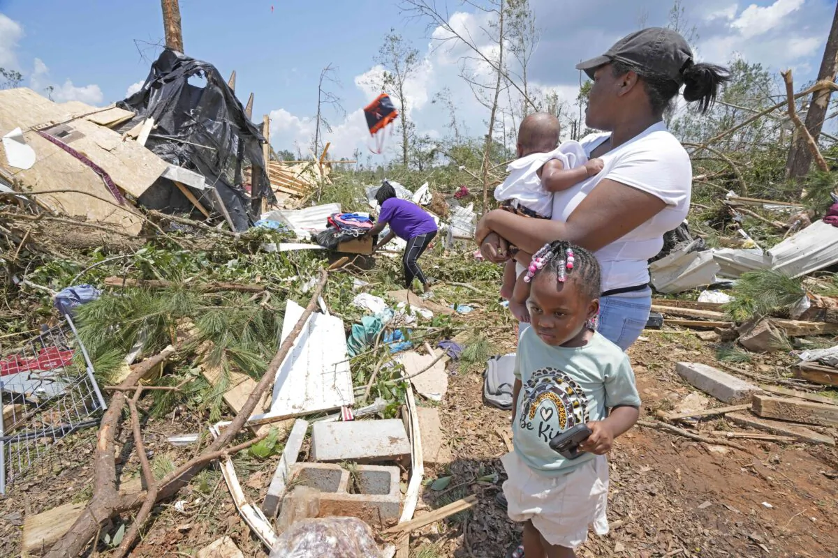 Dana Jackson holds her four month old daughter Brynlee Jackson, while she and daughter Genesis Jackson watch relatives salvage personal items from a relative's mobile home that was demolished by an apparent Sunday night tornado that swept through Louin, Miss., on June 19, 2023. (Rogelio V. Solis/AP Photo)