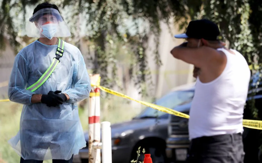 A COVID-19 testing associate dressed in personal protective equipment (PPE) watches a man cough at Lincoln Park in Los Angeles, Calif., on July 7, 2020. (Mario Tama/Getty Images)