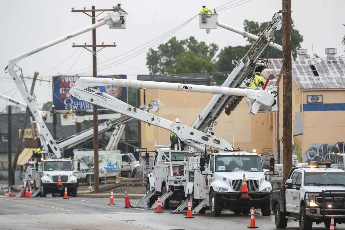 Line workers in boom trucks and on the street work to replace broken utility poles and lines as rain moves in on Peoria Avenue over the Broken Arrow Expressway in Tulsa, Okla., on June 21, 2023. (Daniel Shular/Tulsa World via AP)