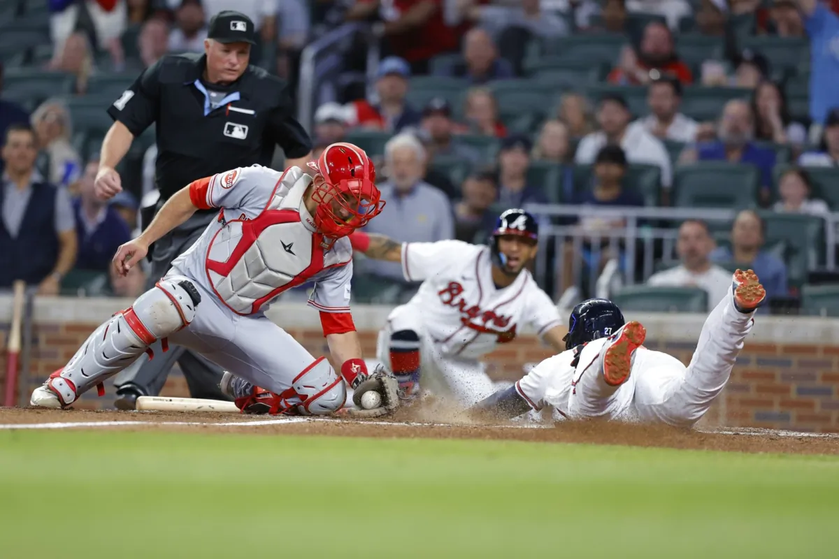 Austin Riley (27) of the Atlanta Braves slides in to score while beating the tag of Luke Maile (22) of the Cincinnati Reds during the third inning at Truist Park in Atlanta, Georgia on April 12, 2023. (Todd Kirkland/Getty Images)
