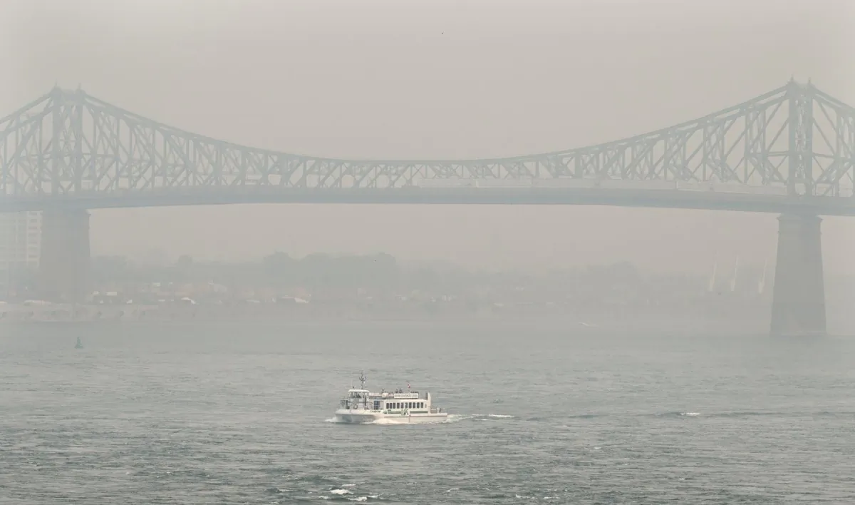A boat passes by the Jacques Cartier bridge obscured by a haze of smog in Montreal, June 25, 2023, as a smog warning is in effect for the city and multiple regions of the province due to forest fires. (The Canadian Press/Graham Hughes)