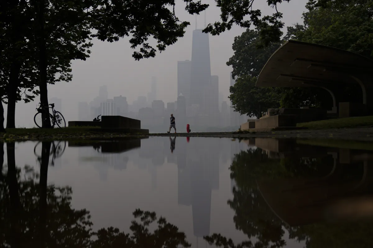 A person walks along the shore of Lake Michigan as the downtown skyline is blanketed in haze from Canadian wildfires in Chicago on June 27, 2023. (Kiichiro Sato/AP Photo)
