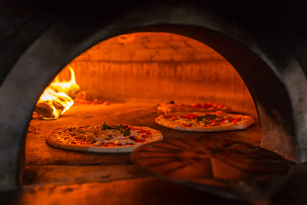 File photo of pizza pies in a wood oven. (Mazur Travel/Shutterstock)