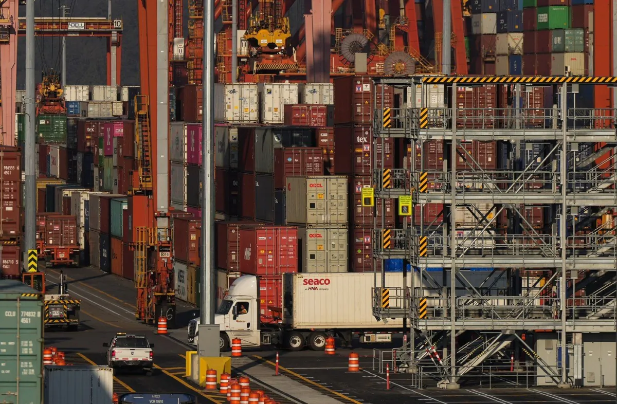 A truck carries a cargo container at the Port of Vancouver Centerm container terminal as others are stacked under gantry cranes, in Vancouver, on Oct. 14, 2022. (The Canadian Press/Darryl Dyck)