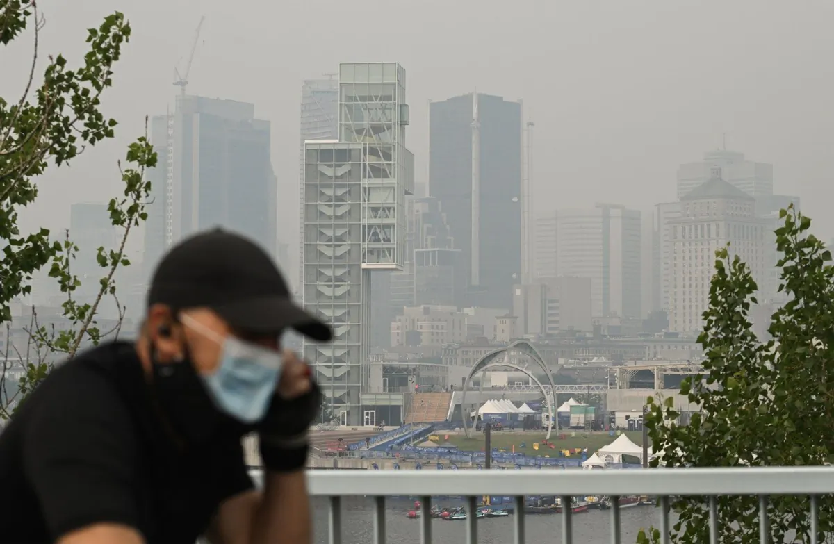 A man wears a face mask as he cycles by the skyline of Montreal, June 25, 2023. (The Canadian Press/Graham Hughes)
