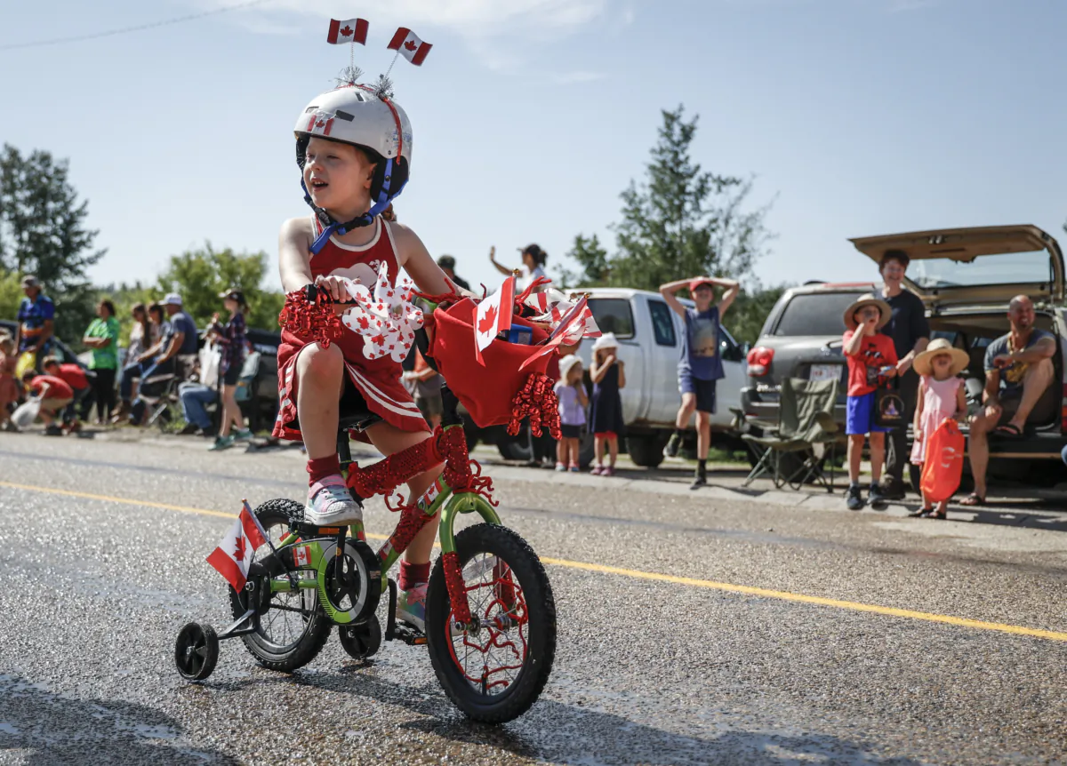 A child rides her bike during a Canada Day parade in Cremona, Alta., on July 1, 2023. (The Canadian Press/Jeff McIntosh)