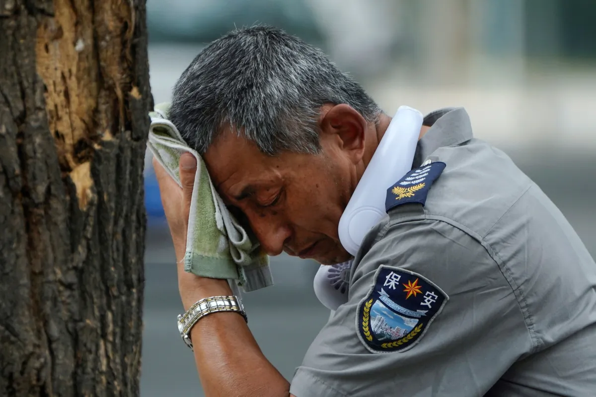 A security guard wearing an electric fan on his neck wipes his sweat on a hot day in Beijing on July 3, 2023. (Andy Wong/AP Photo)