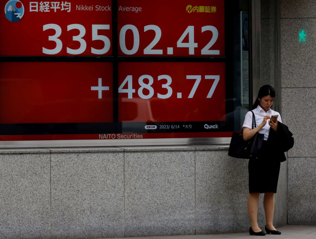 A woman uses a mobile phone in front of an electric board displaying the Nikkei stock average outside a brokerage in Tokyo, Japan, on June 14, 2023. (Kim Kyung-Hoon/Reuters)