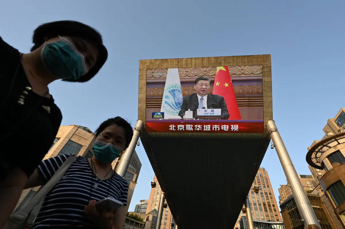 Two women wait below a giant screen showing news footage of Chinese leader Xi Jinping speaking virtually to the Shanghai Cooperation Organization meeting, which was being held in India, at a shopping mall in Beijing on July 4, 2023. (Greg Baker/AFP via Getty Images)