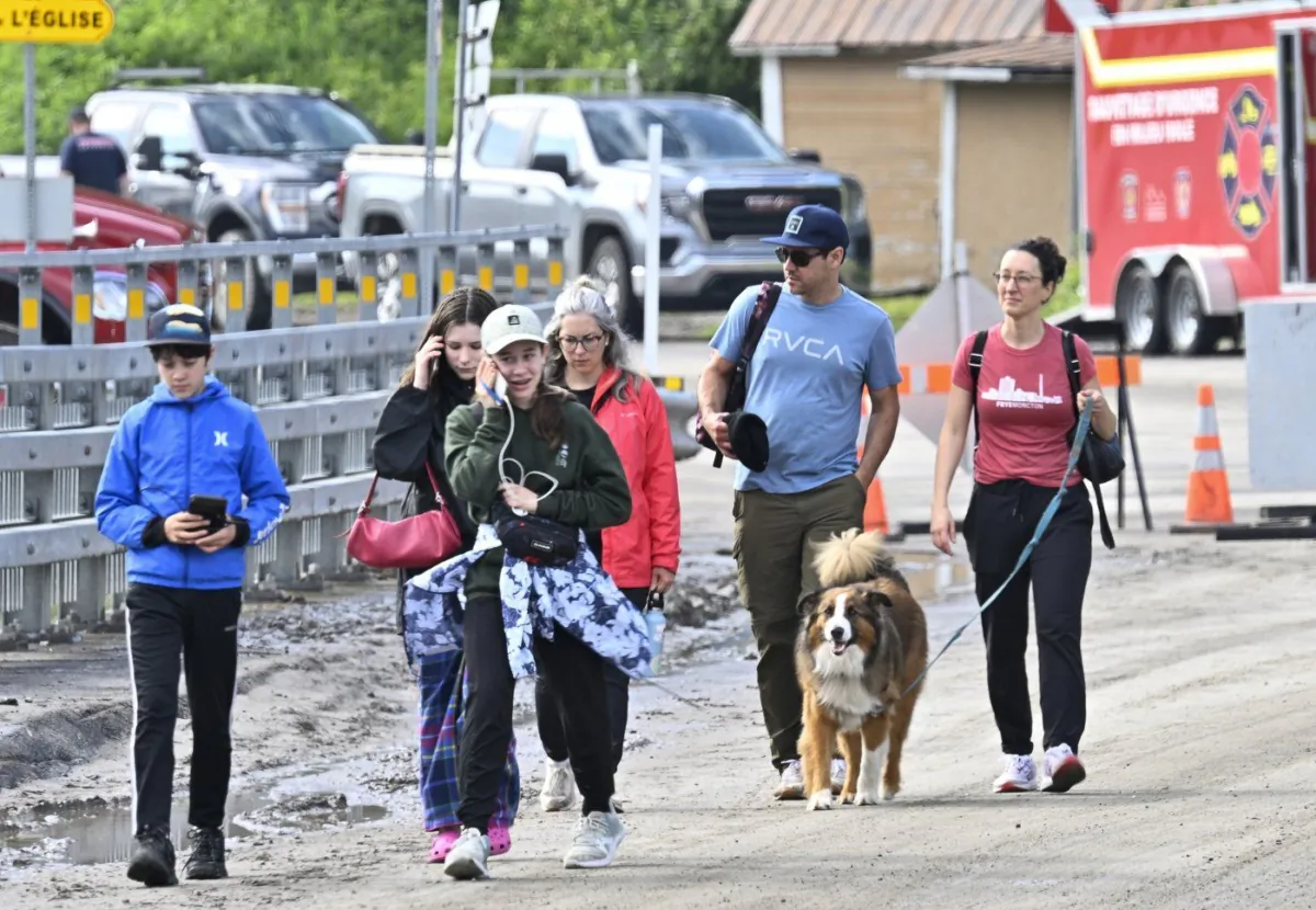 People walk to city hall with their dog after they were evacuated from a campground, in Rivière-Éternité, Que., on July 2, 2023. (The Canadian Press/Jacques Boissinot)