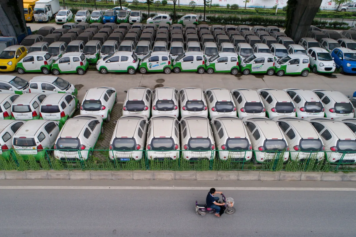 A motorist rides past new electric vehicles parked in a parking lot under a viaduct in Wuhan, Hubei Province, China, on May 22, 2017. (STR/AFP via Getty Images)