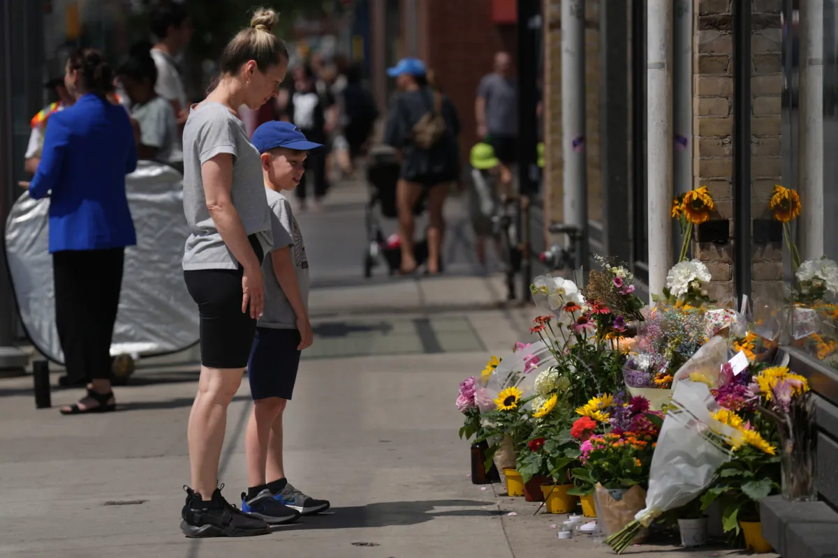 Passersby stop at a makeshift memorial at the place where a mother of two, Karolina Huebner-Makurat, was killed by a stray bullet, in Toronto on July 10, 2023. (The Canadian Press/Chris Young)