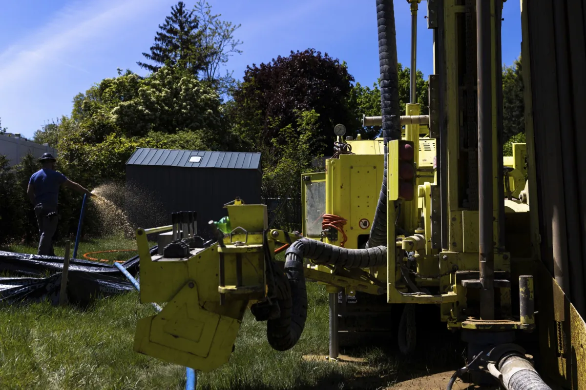 A Dandelion Energy employee sprays excess groundwater back on the lawn during installation of a geothermal heat pump system at a home in White Plains, N.Y., on May 8, 2023. (Julia Nikhinson/AP Photo)