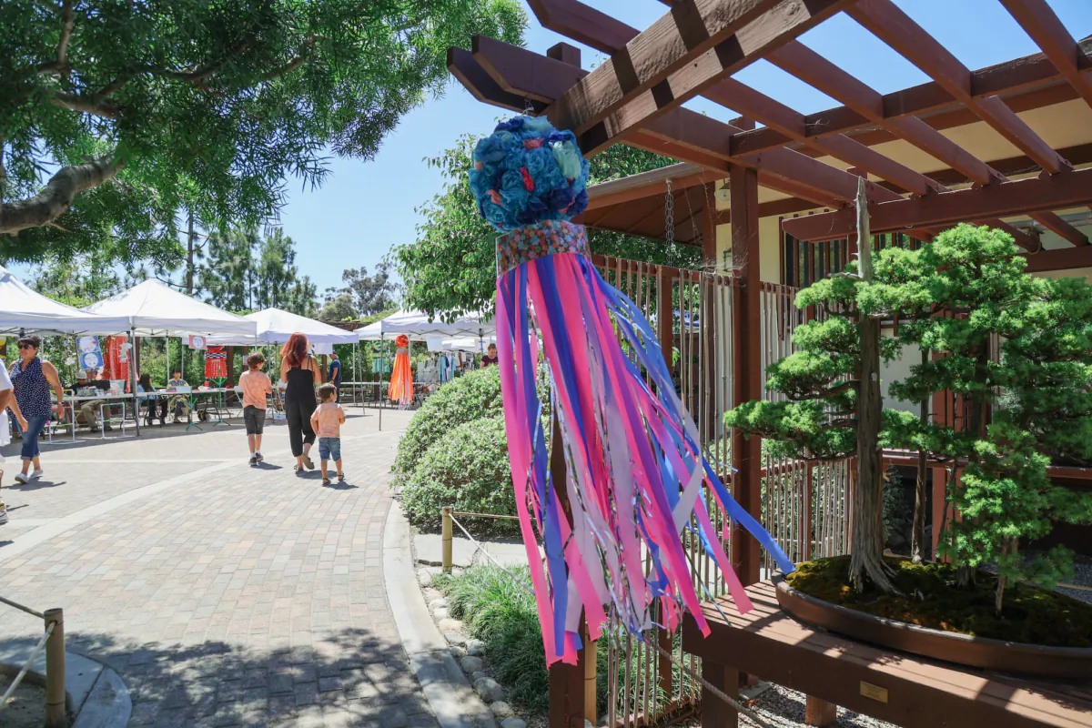 A Fukinagashi, streamer decorations of fabric, hangs over bonsai trees at the Tanabata Festival in the Balboa Park Japanese Friendship Garden in San Diego, Calif., on July 7, 2023. (Julianne Foster/The Epoch Times)