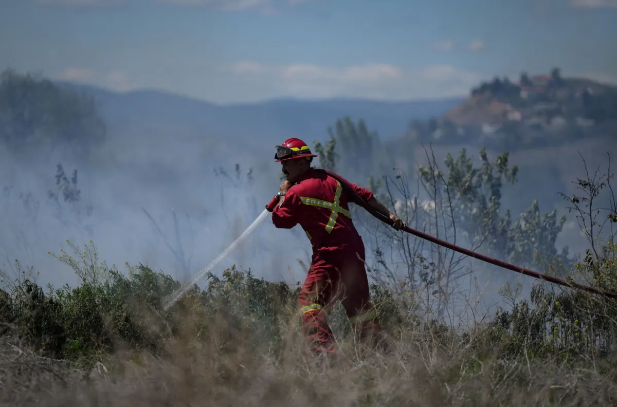 A firefighter directs water on a grass fire burning on an acreage behind a residential property in Kamloops, B.C., on June 5, 2023. (The Canadian Press/Darryl Dyck)