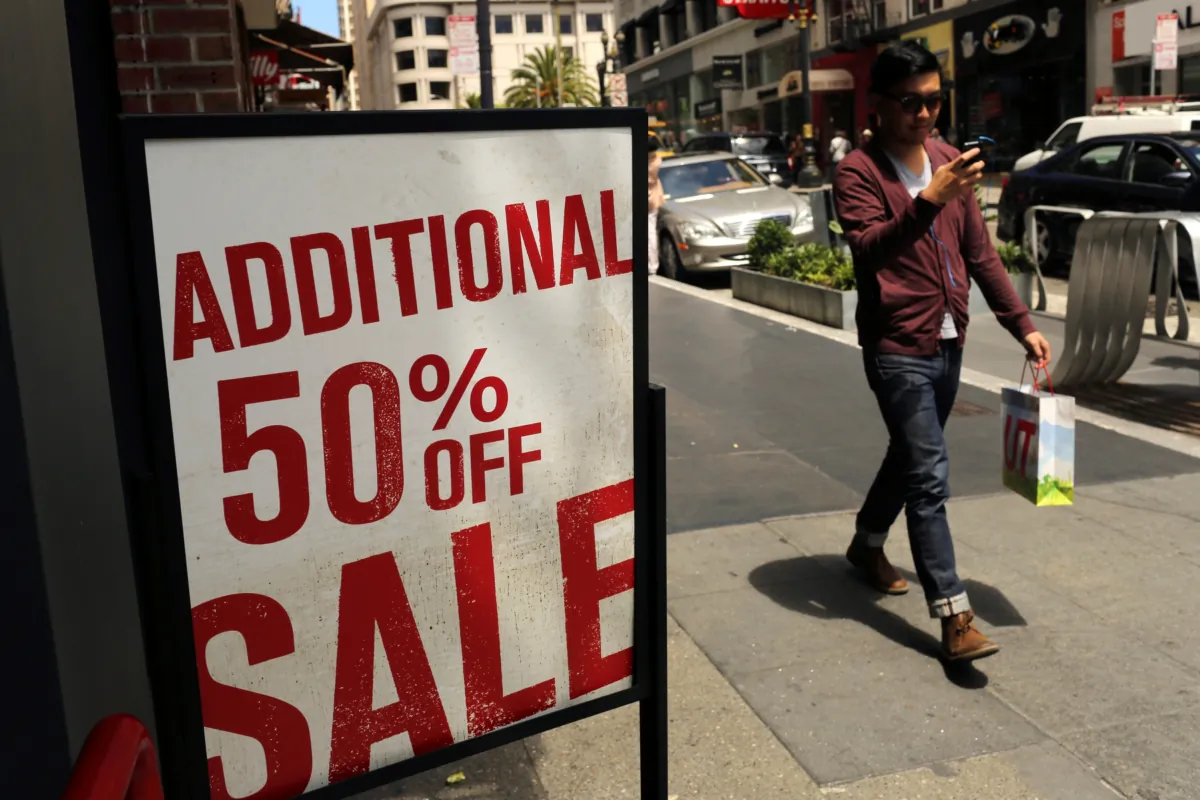 A man with a shopping bag walks past a sale sign at a retail clothing store in San Francisco on May 13, 2013. (Robert Galbraith/Reuters)