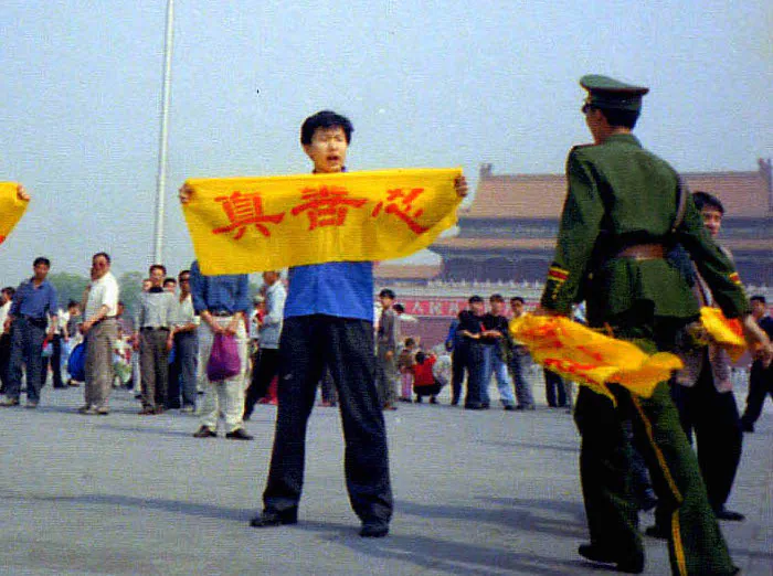 A Chinese policeman approaches a Falun Gong practitioner at Tiananmen Square in Beijing as he holds a banner with the Chinese characters for "truthfulness, compassion, and tolerance," the core tenets of Falun Gong. (Courtesy of Minghui.org)