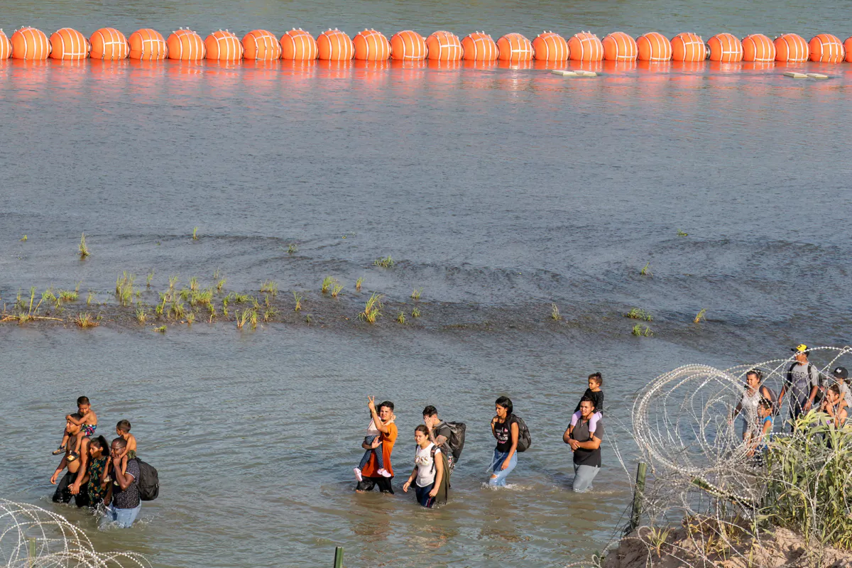 Illegal immigrants walk between concertina wire fencing and a string of buoys placed on the water along the Rio Grande border with Mexico in Eagle Pass, Texas, on July 16, 2023. (Suzanne Cordeiro/AFP/Getty Images)
